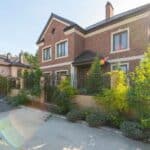 Elegant brick house with a lush garden and driveway, under a clear sky