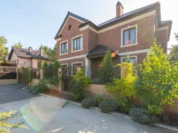 Elegant brick house with a lush garden and driveway, under a clear sky